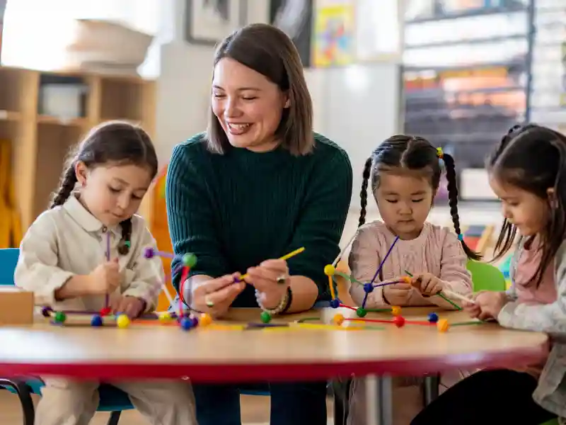 Happy teacher sitting with smiling children at a school table.