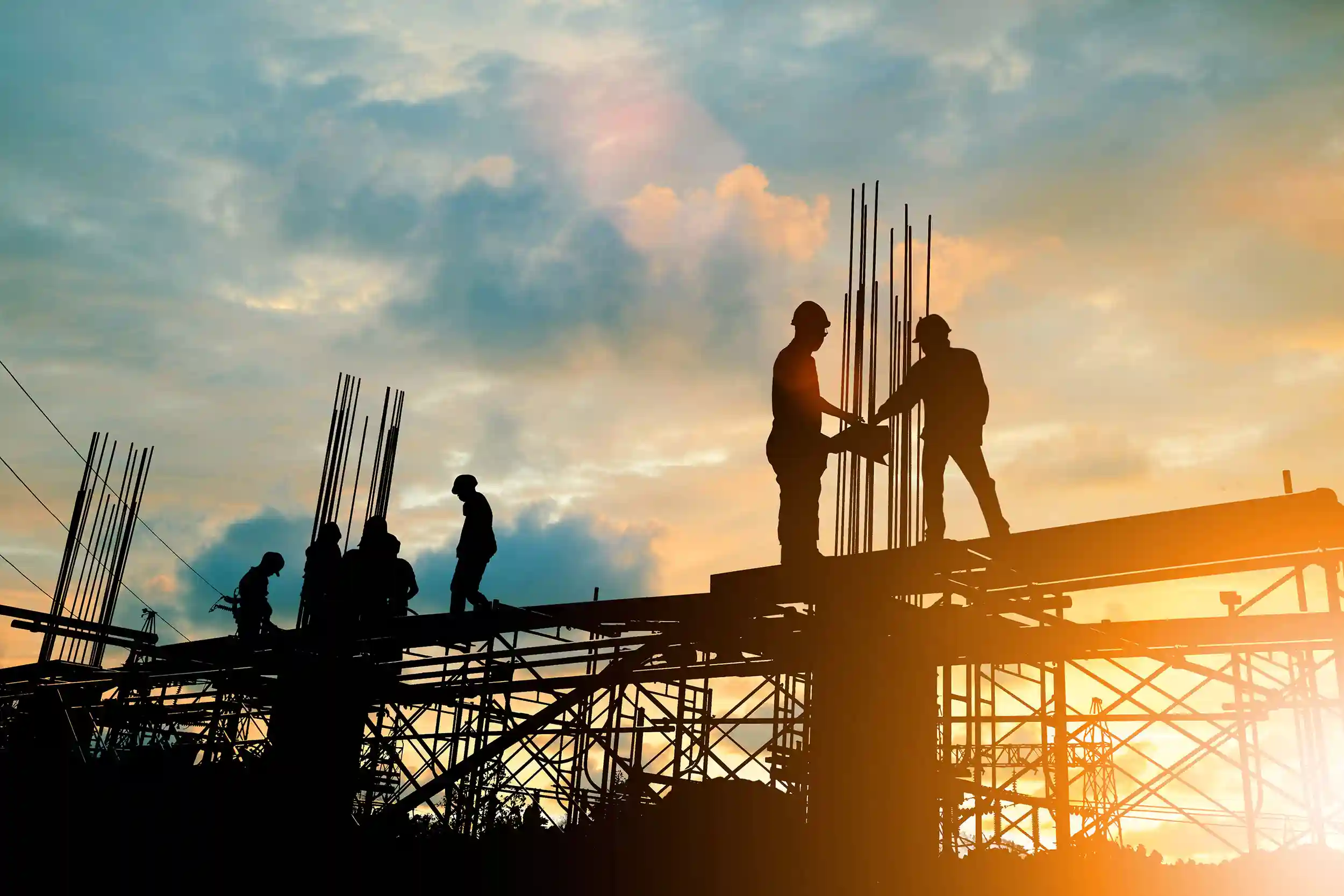 Workers inspect rebar at a construction site in the early morning sunrise.