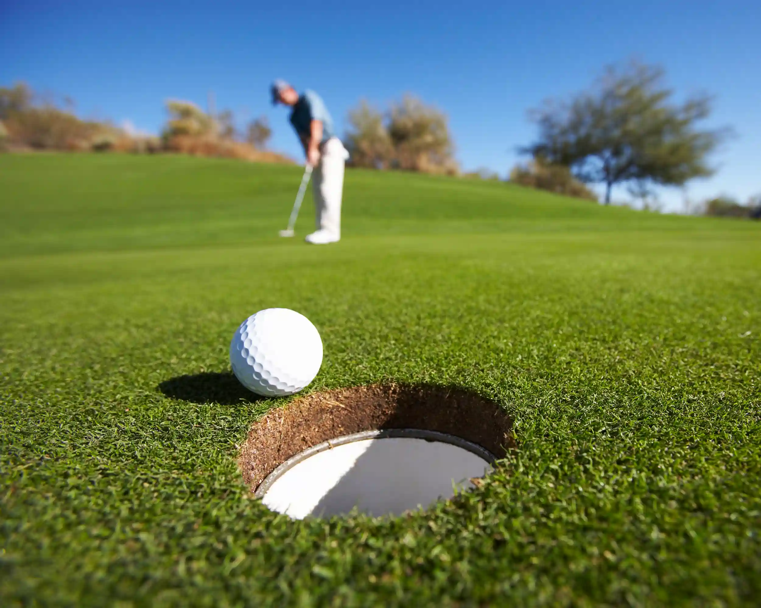 A close up of a golf ball rolling into the hole on a putting green with the golfer in the background.