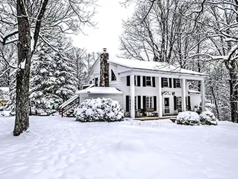 Large white house in the woods on a snowy day.