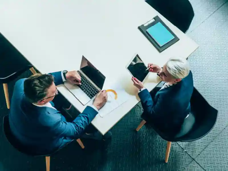 Two people talking at a table with a laptop and tablet