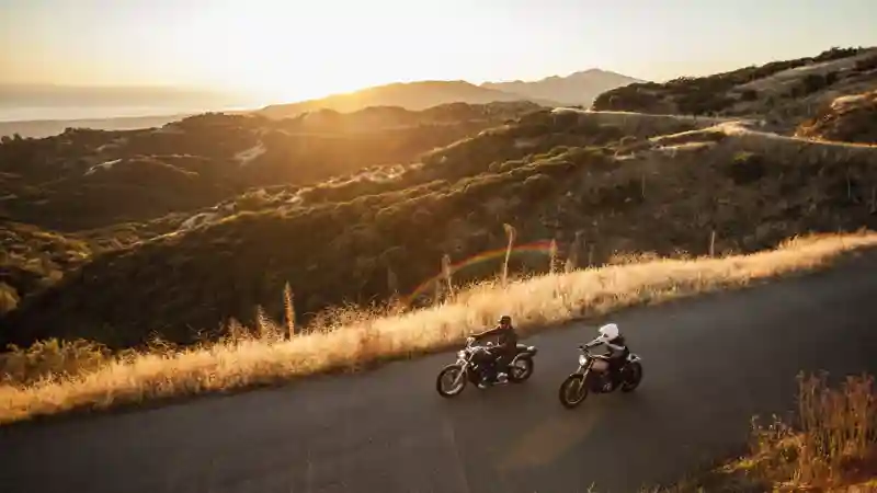 Two individuals riding motorcycles side by side on a scenic road, showcasing freedom and adventure.