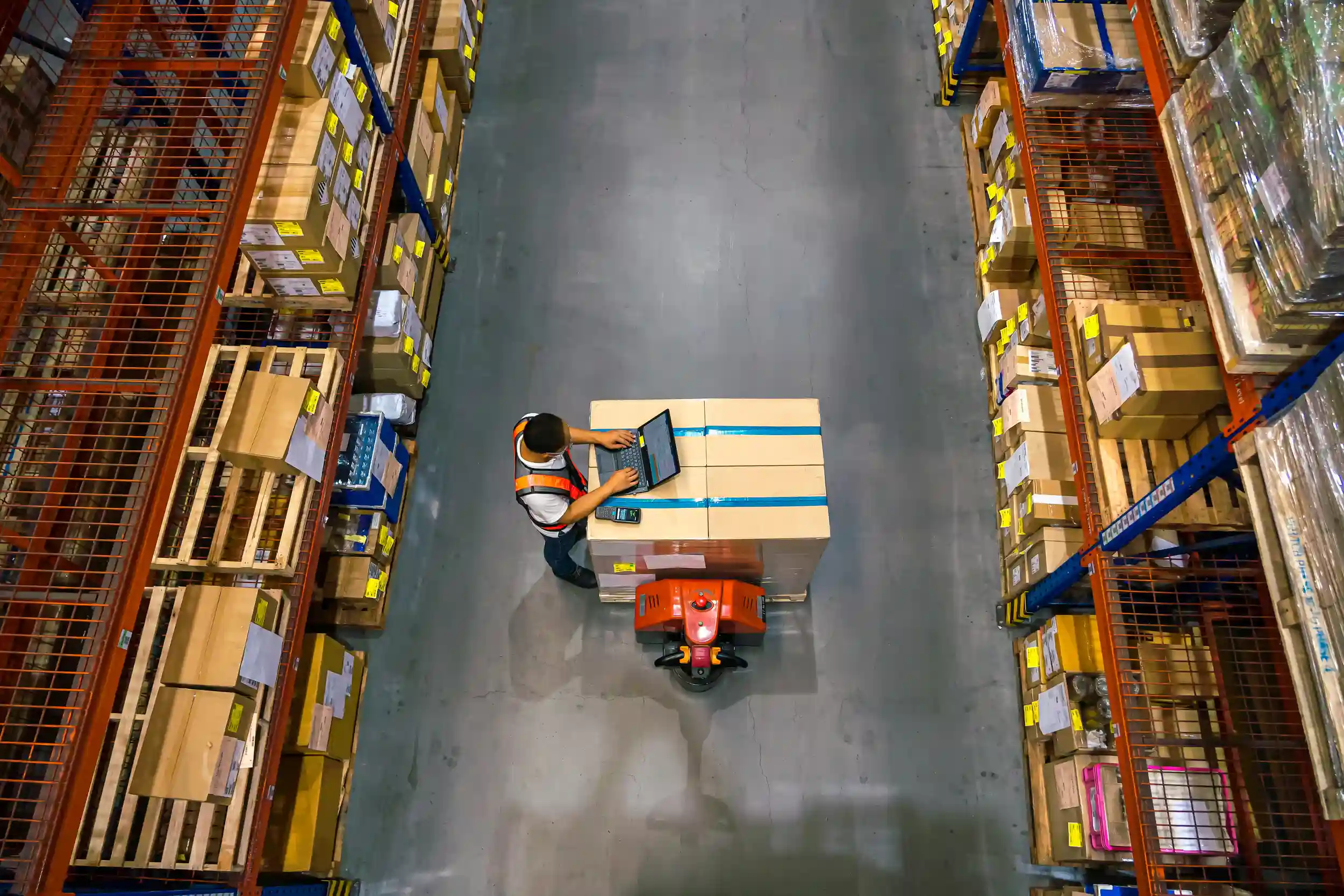 A person on a laptop in the middle of a warehouse around multiple inventories.