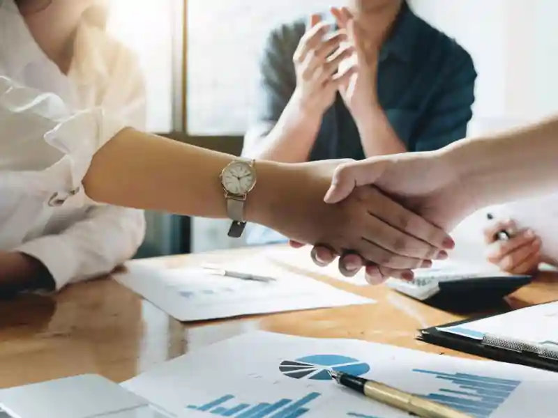 Two people shaking hands with another clapping in the background