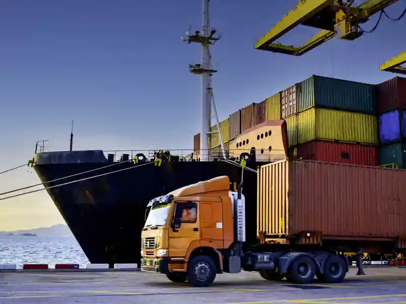 A truck driving past a cargo ship loaded with containers.