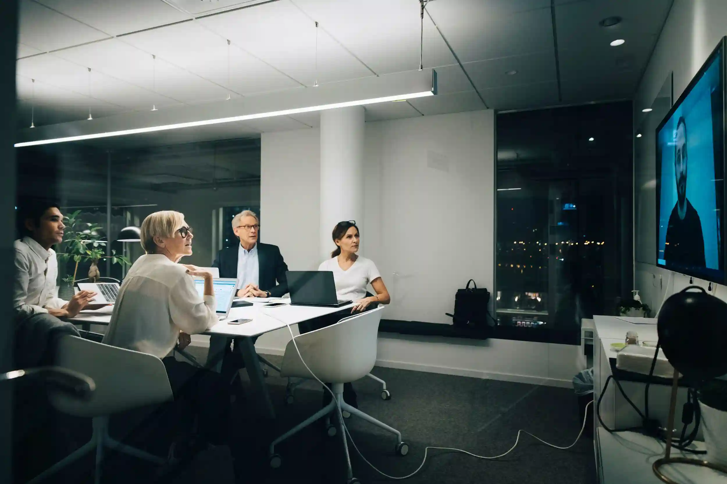 Colleagues looking at businessman during video conference meeting at night in office