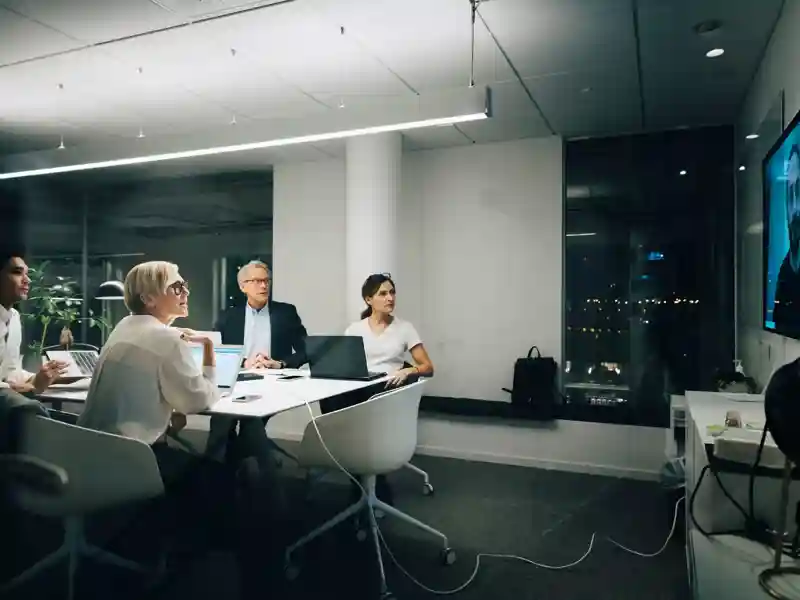 Colleagues looking at businessman during video conference meeting at night in office
