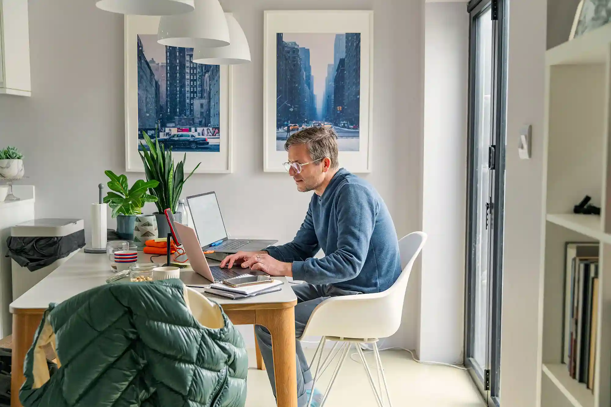 A casually-dressed man works on two laptops in a home office